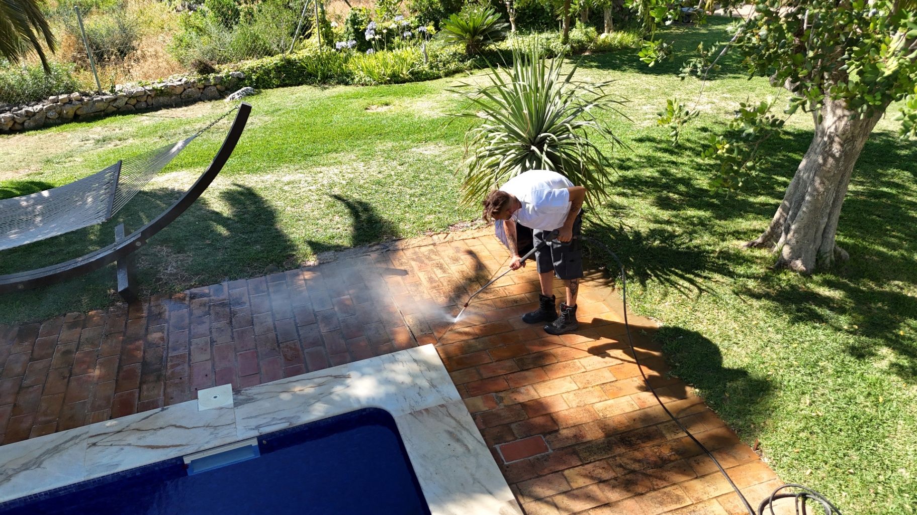 Close-up of pressure washing terracotta patio tiles beside a private pool in the Algarve, Portugal